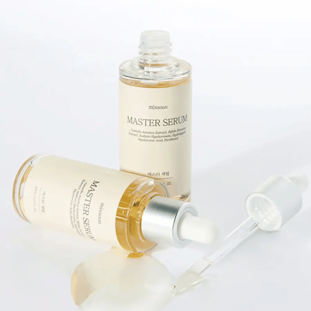 Dve steklenički Mixsoon Master Serum, ena stoječa in ena ležeča z odprto pipeto, kjer se je serum razlil po beli površini.