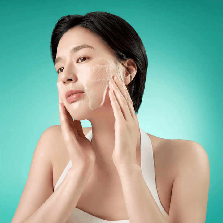 Ženska čisti obraz z blagim penastim čistilnim peno za obraz na zeleni podlagi.