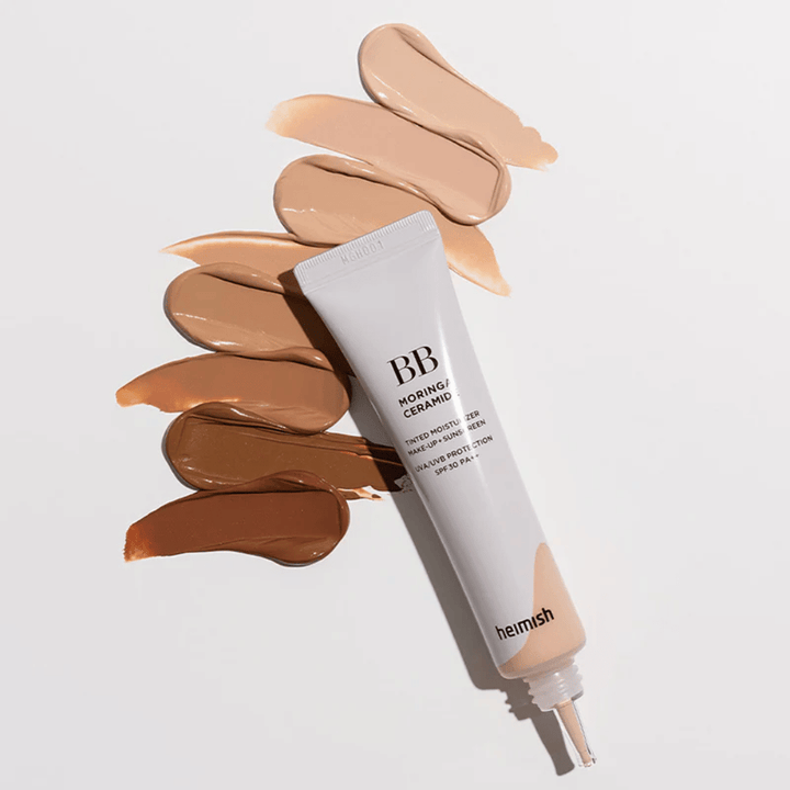 Heimish Moringa Ceramide BB Cream obkrožen z več vzorci odtenkov v različnih tonih kože. Slika prikazuje široko barvno paleto izdelka in kremasto teksturo, ki zagotavlja naravno prekrivnost in enakomeren ten kože.