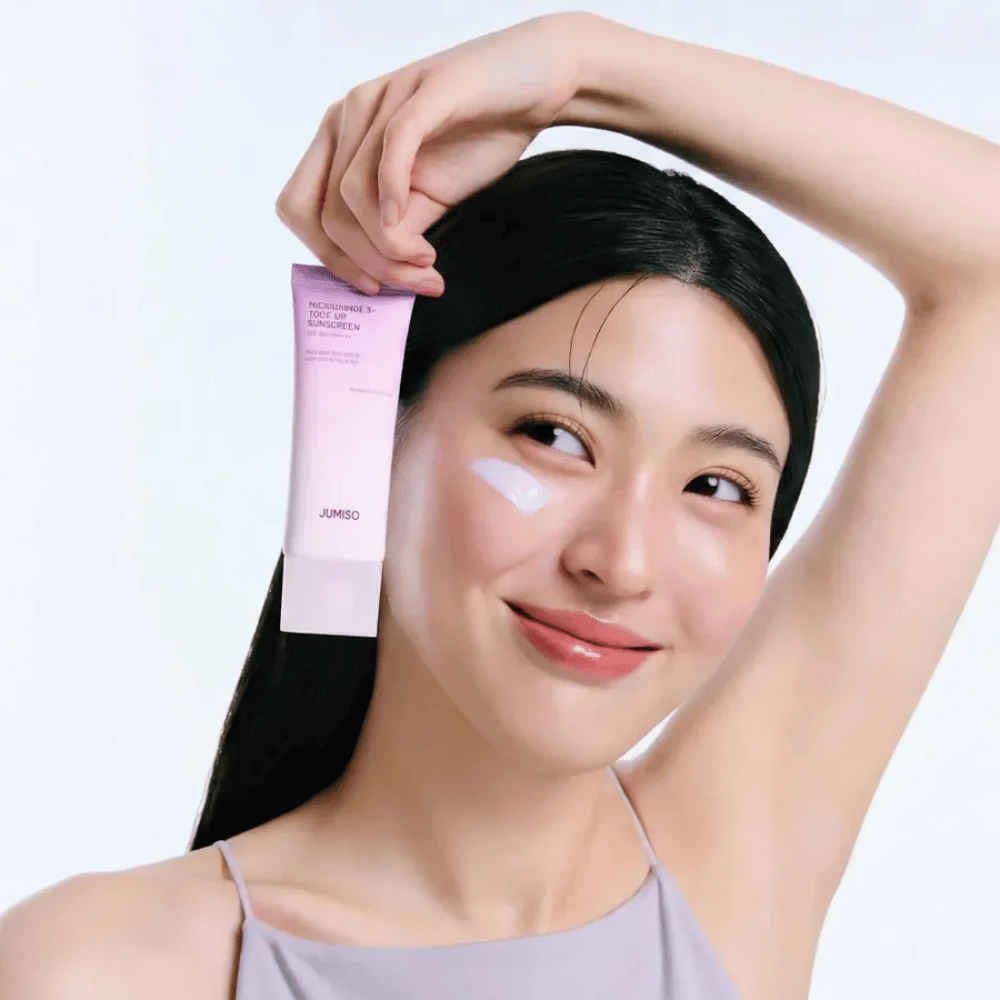 Model drži JUMISO Niacinamide 3+ Tone-Up Sunscreen SPF50+ PA++++ – kremo za sončenje z niacinamidom, ki izenači ten kože in ščiti kožo.