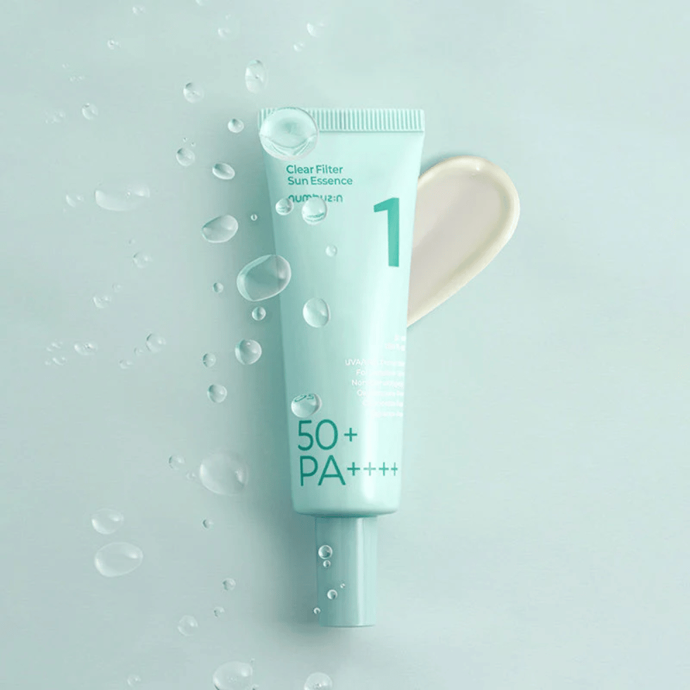 Svetlo modra tuba z No.1 Clear Filter Sun Essence SPF 50+ PA++++. Tuba je okrašena z vodnimi kapljicami in poleg je prikazan klik izdelka. Izdelek je zasnovan za zagotavljanje visoke zaščite pred soncem in zaščito pred UVA/UVB žarki.