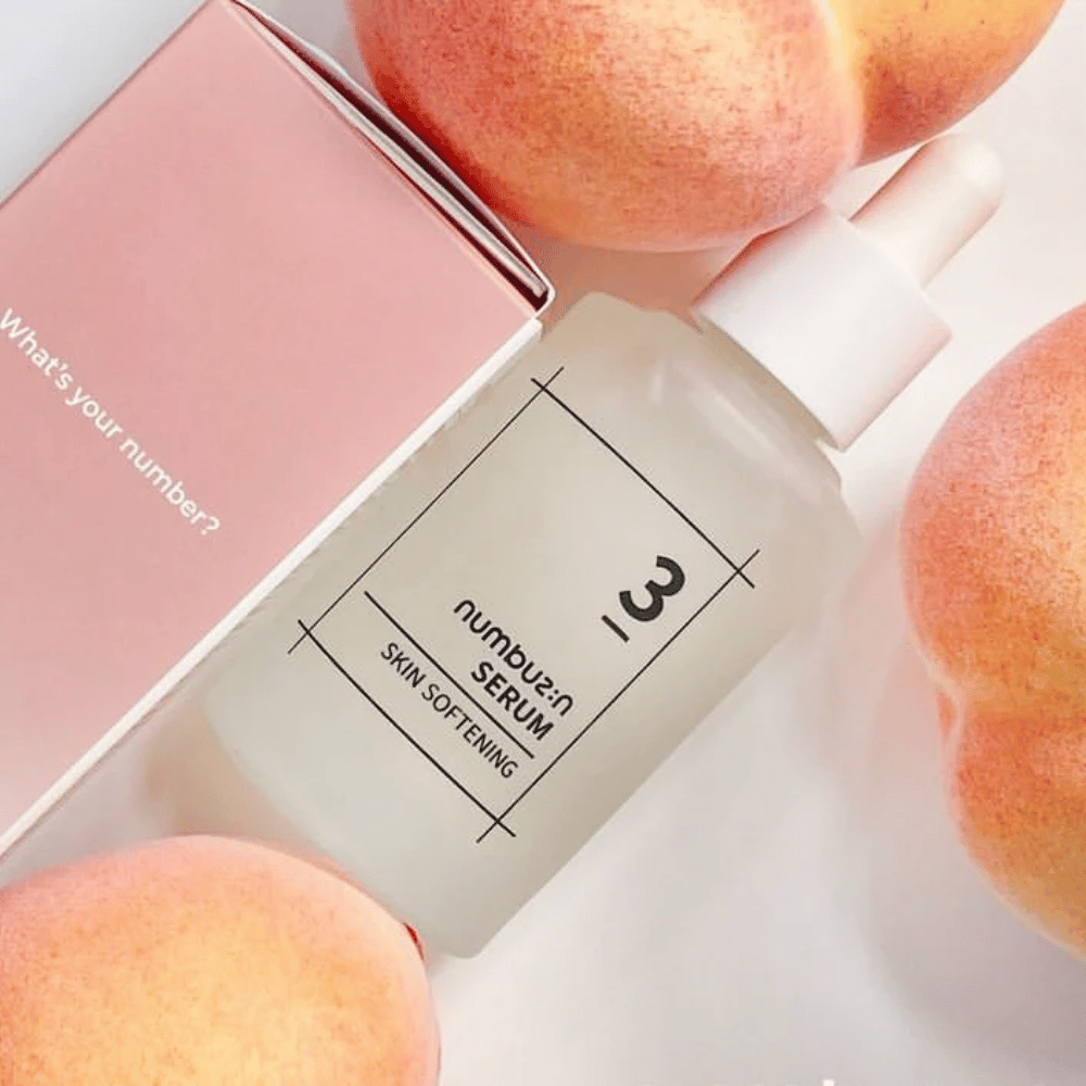 Steklenička z numbus:in No.3 Serumom za mehčanje kože, obdana z breskvami in rožnato škatlo z napisom "Katera je tvoja številka?".