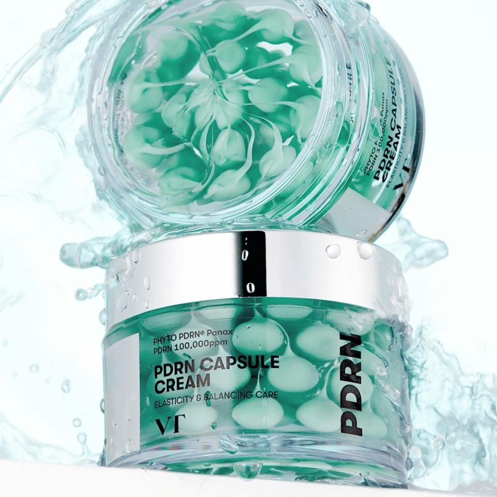 Dve posodi VT PDRN Capsule Cream zloženi s kapljicami vode okrog njih. Prosojne posode prikazujejo zelene kapsule znotraj, z besedilom "Elasticity & Balancing Care" vidnim na oznaki.