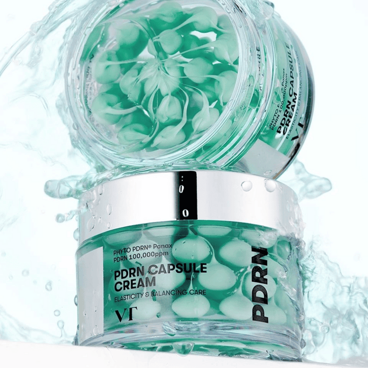 Dve posodi VT PDRN Capsule Cream zloženi s kapljicami vode okrog njih. Prosojne posode prikazujejo zelene kapsule znotraj, z besedilom "Elasticity & Balancing Care" vidnim na oznaki.