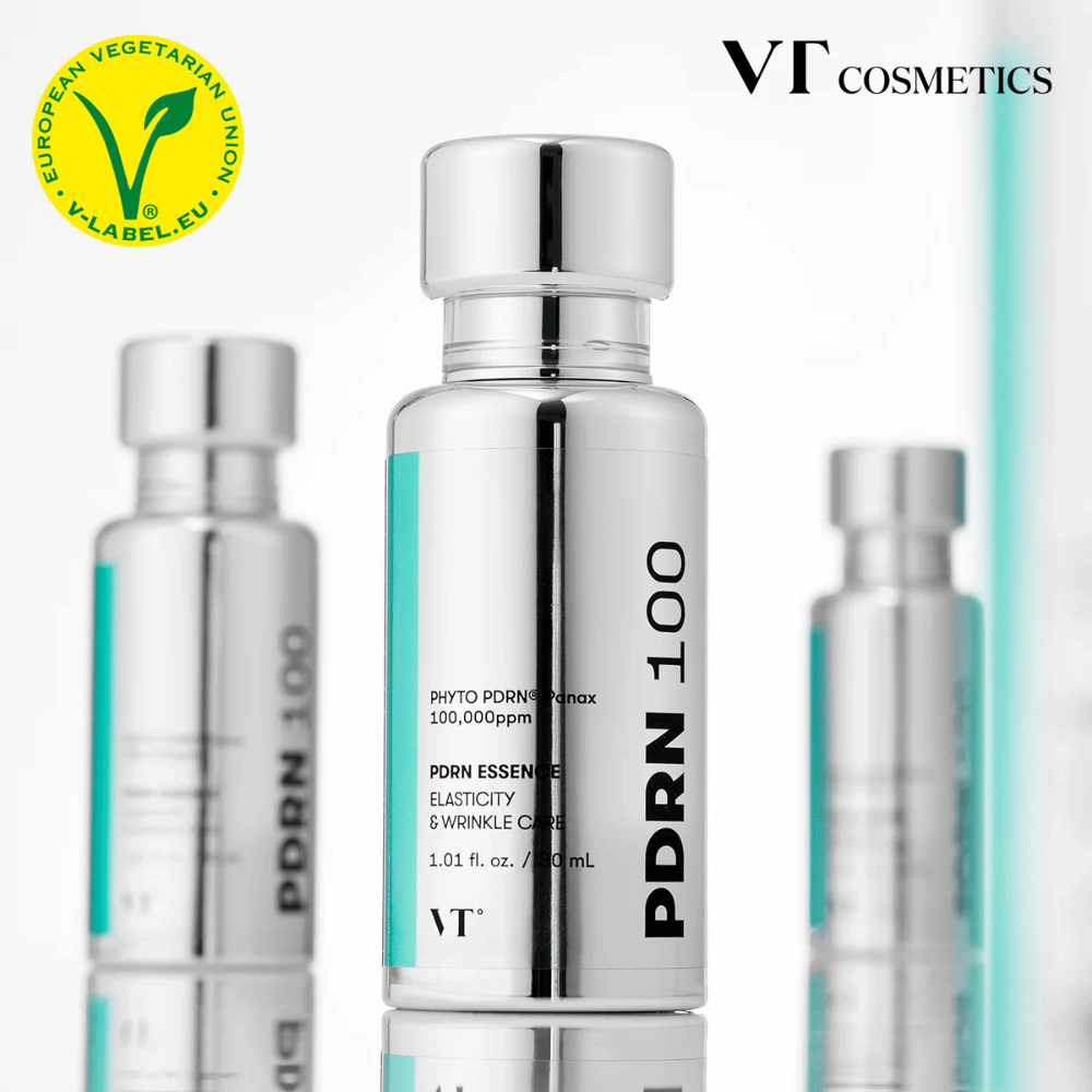 Več srebrnih stekleničk VT PDRN 100 Essence je postavljenih v vrsto, z jasno označbo 100.000 ppm PDRN in poudarkom na elastičnosti in negi gub. Na vrhu je logotip VT Cosmetics in oznaka V-label za vegetarijansko vsebino.