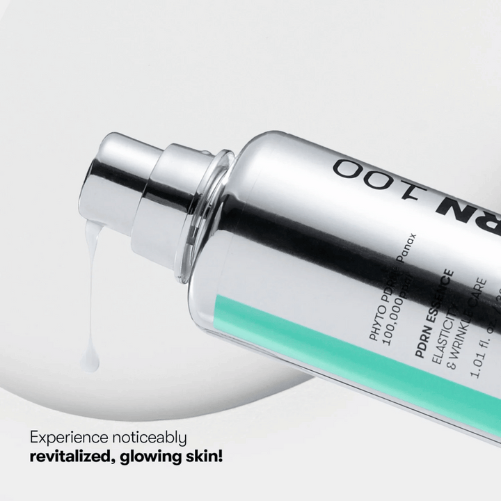 Bližnji posnetek srebrne stekleničke s pumpico VT PDRN Essence 100. Bela esenca teče iz šobe, besedilo na sliki pa pravi: "Doživite vidno revitalizirano, sijočo kožo!"