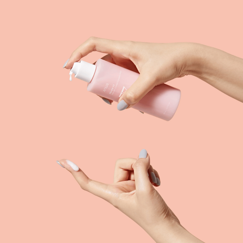 Slika prikazuje nečije roke, ki držijo steklenico ANUA Peach 77% Niacin Conditioning Milk. Ta izdelek za nego kože ima mlečno konsistenco in je zasnovan za nego in izboljšanje stanja kože.