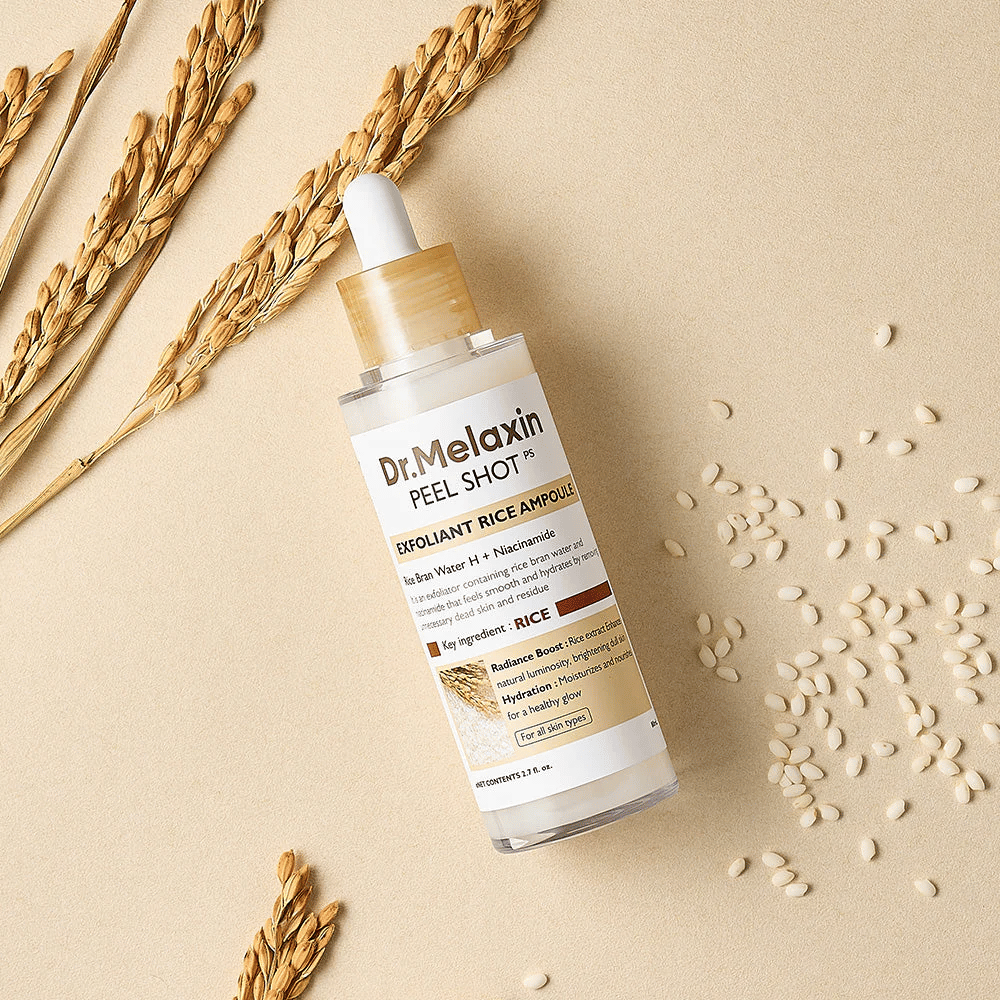 Dr.Melaxin Peel Shot Rice Ampoule leži na peščeni površini z rižem in klasjem, eksfoliantna ampula za obraz, ki združuje blago luščenje z intenzivno vlago.