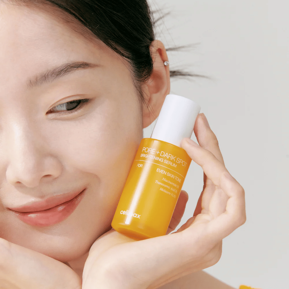 Model drži Celimax Pore + Dark Spot Brightening Serum blizu obraza, prikazuje sijočo kožo.