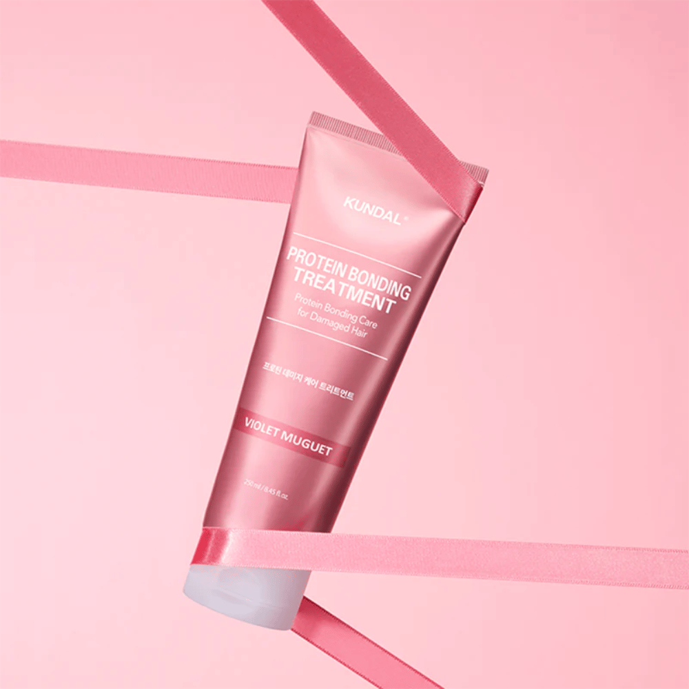 KUNDAL Protein Bonding Treatment Violet Muguet v roza tubi 250 ml pred rožnatim ozadjem z dekorativnimi trakovi.