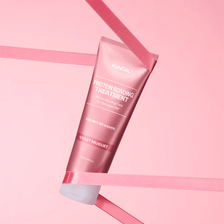KUNDAL Protein Bonding Treatment Violet Muguet v roza tubi 250 ml pred rožnatim ozadjem z dekorativnimi trakovi.