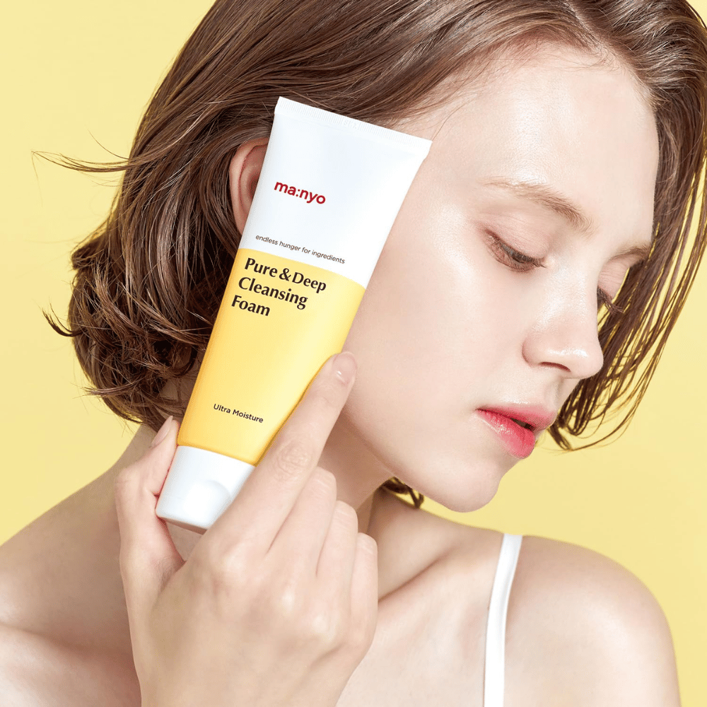 Ženska z zdravo, navlaženo kožo drži Ma:nyo Pure & Deep Cleansing Foam – nežen čistilec obraza, ki daje sijaj in ravnovesje z naravnimi sestavinami.