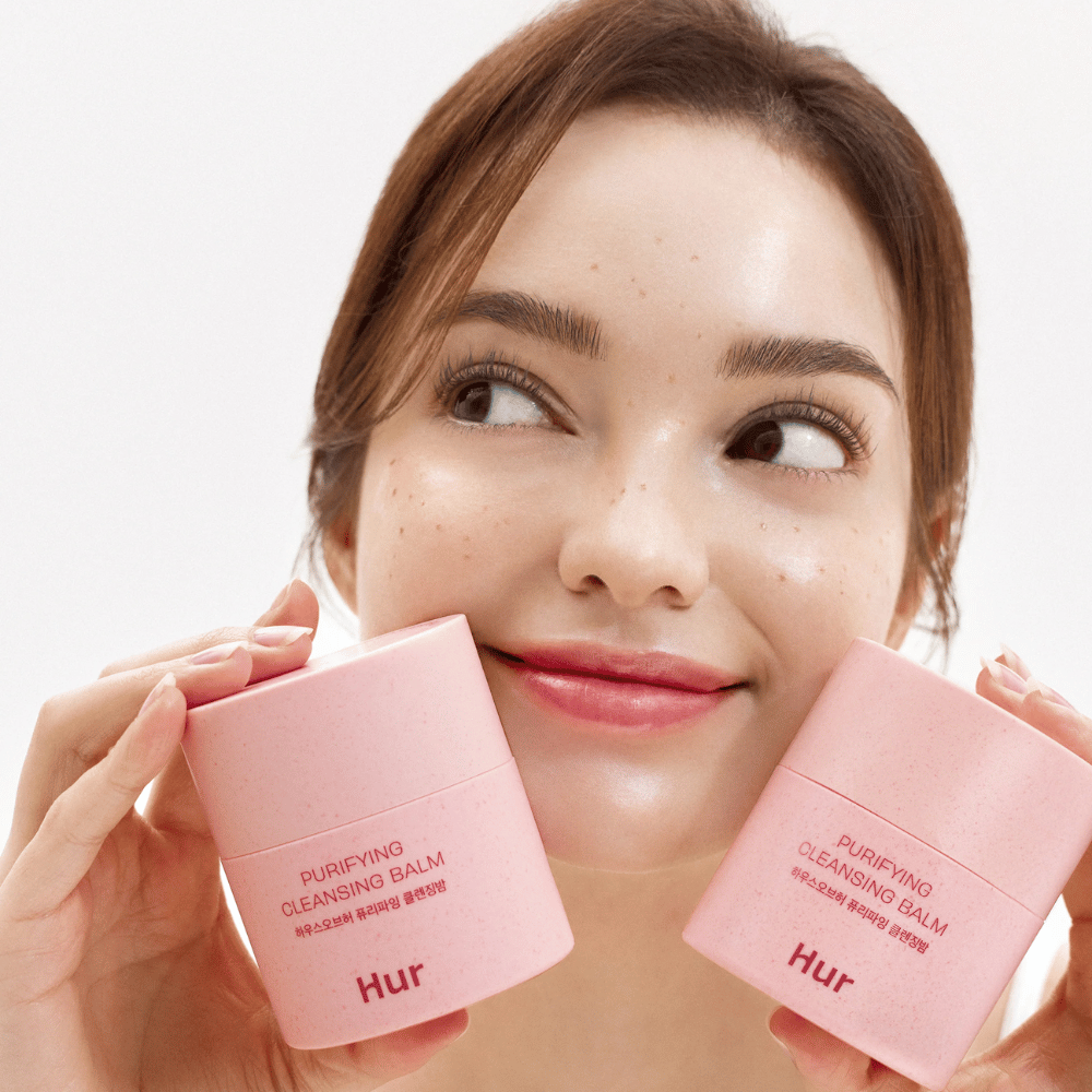 Model drži dva lončka Kako Purifying Cleansing Balm. Nežen čistilni balzam, ki je primeren za občutljivo kožo in daje svež, navlažen občutek po čiščenju.