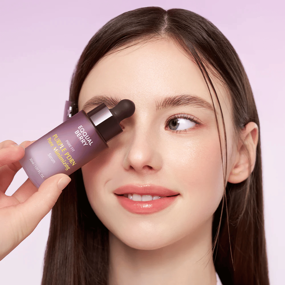 Mlada ženska z gladko kožo drži stekleničko Equal Berry Purple PDRN Pore Minimizing Serum ob čelu, na svetlo vijoličnem ozadju.