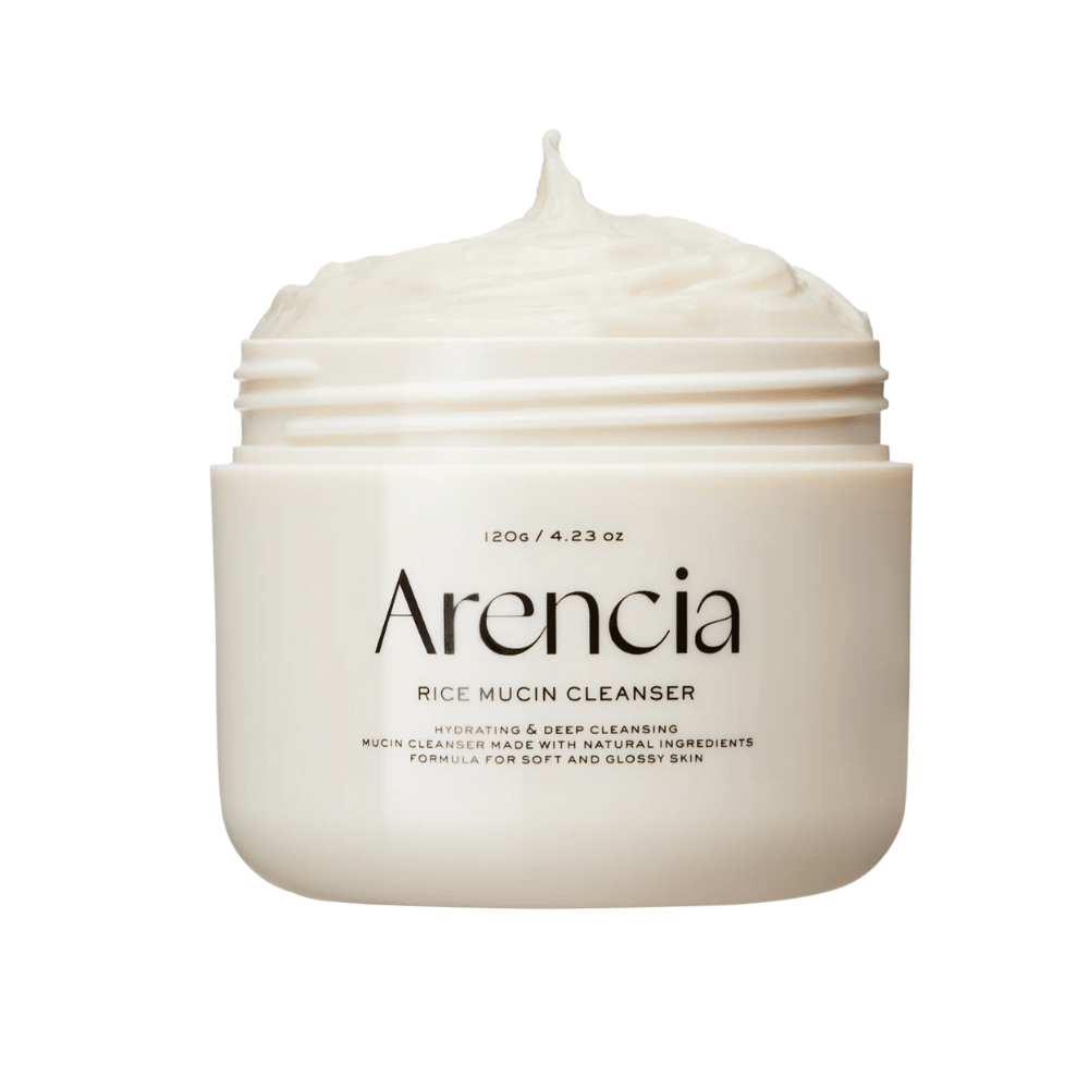 Slika izdelka Arencia Rice Mucin Cleanser v beli posodi s kremasto, stepeno teksturo, ki štrli iz odprtine. Besedilo na embalaži poudarja vlaženje in globinsko čiščenje.