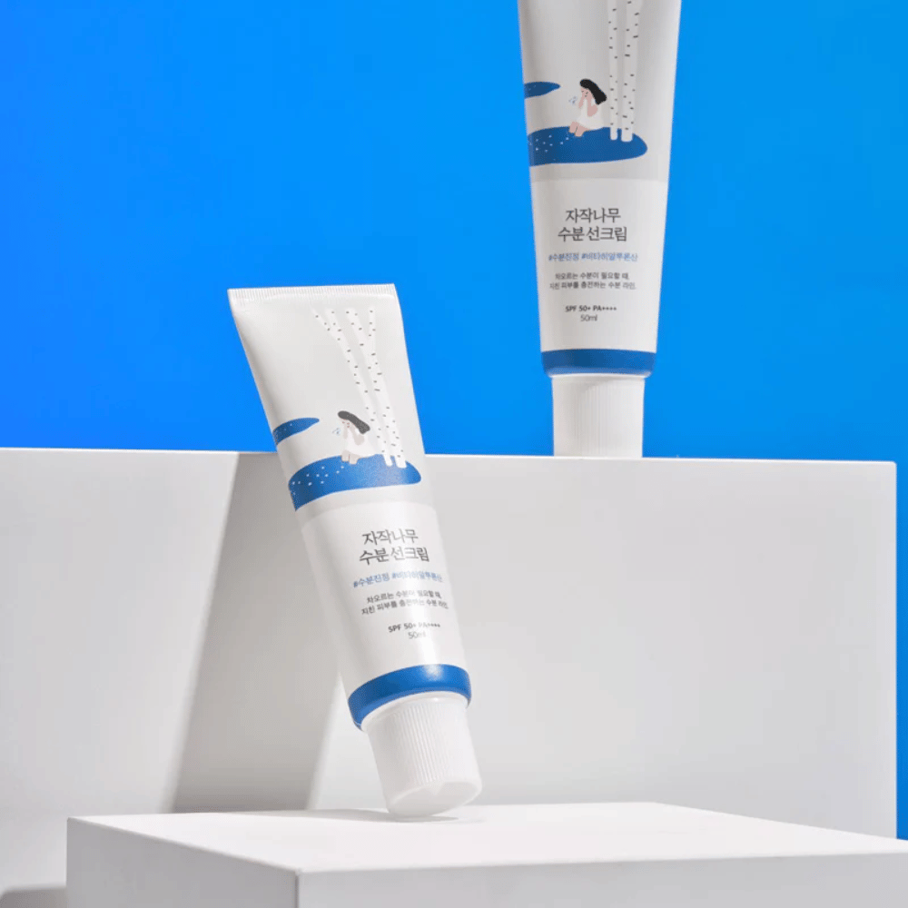 Dve tubi z Round Lab Birch Juice Moisturizing Sunscreen SPF50+ PA++++ 50ml, ki sta na modrem ozadju.