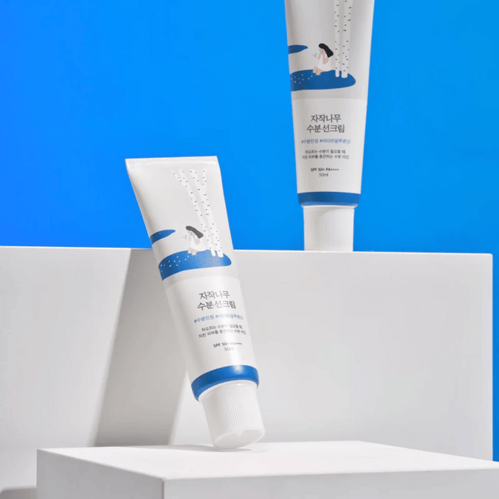 Dve tubi z Round Lab Birch Juice Moisturizing Sunscreen SPF50+ PA++++ 50ml, ki sta na modrem ozadju.