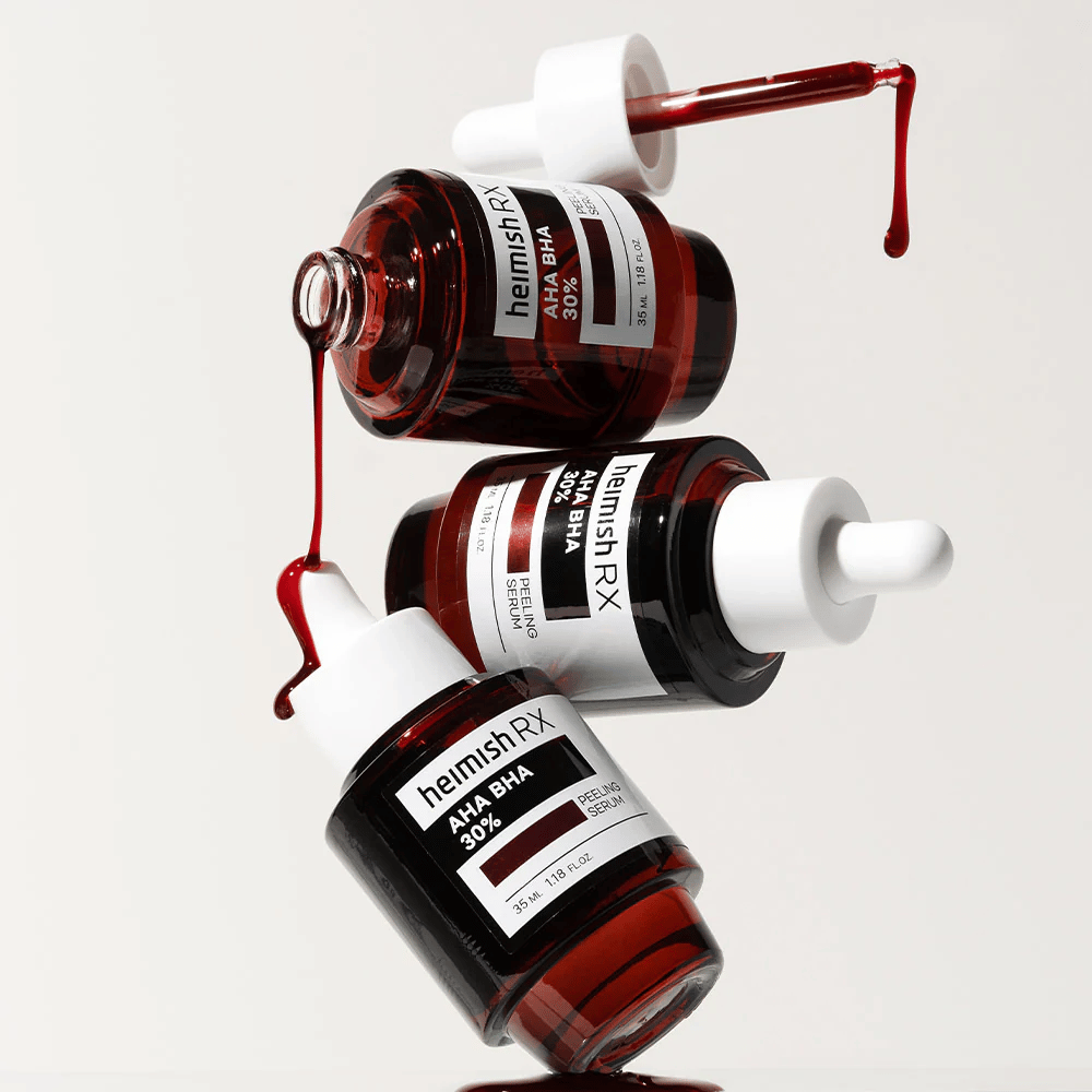 Tri stekleničke Heimish RX AHA BHA 30% Peeling Serum v dinamični kompoziciji, z rdečim serumom, ki kaplja iz pipet.