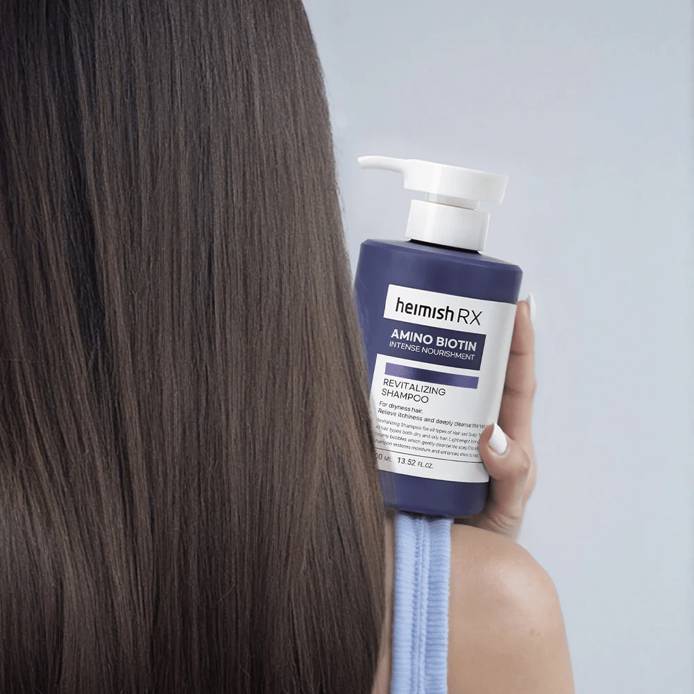 Heimish RX Amino Biotin Revitalizing Shampoo drži v roki proti dolgim, sijočim lasem – prikazuje rezultat intenzivne prehrane in vlaženja za suhe lase.