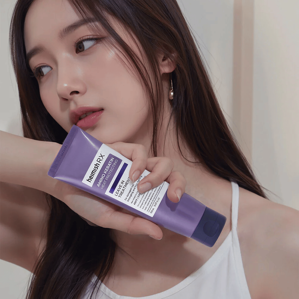 Ženska z dolgimi, sijočimi lasmi drži Heimish RX Amino Keratin Leave-In Treatment – prikazuje izdelek kot negovalni in toplotno zaščitni korak v rutini za nego las.