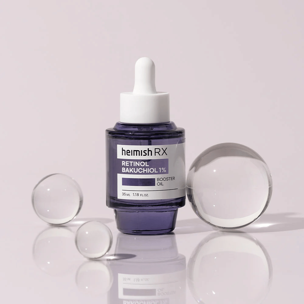 Heimish RX Retinol Bakuchiol Booster Oil 1% v elegantni vijolični steklenički s pipeto. Olje je postavljeno na odsevno površino z okoliškimi steklenimi kroglicami, kar daje občutek razkošja in modernosti.