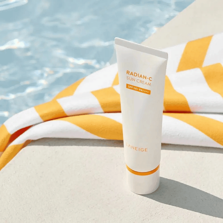 LANEIGE Radian-C Sun Cream stoji ob robu bazena z rumeno-belim črtastim brisačo v ozadju.