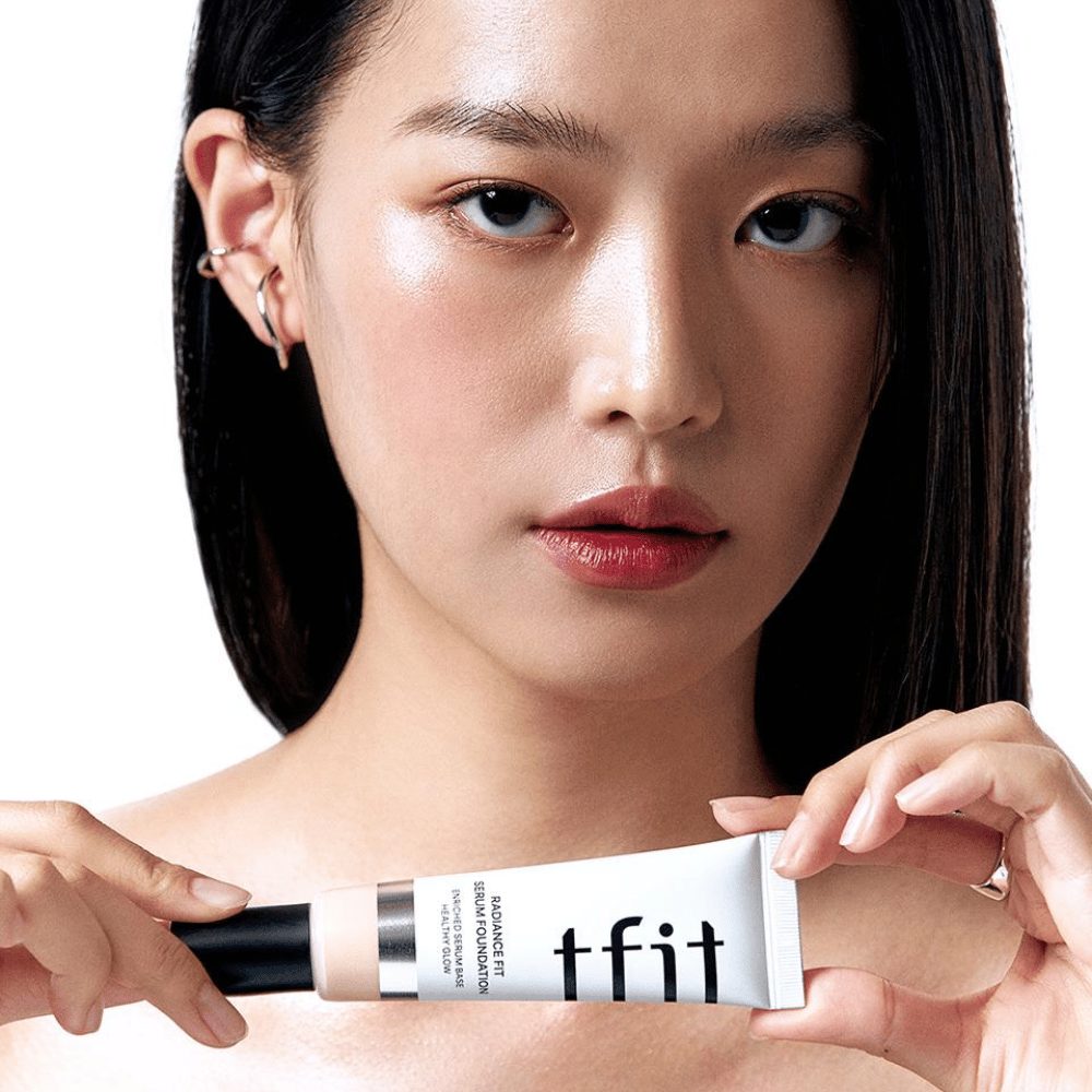 Model z sijočo, gladko kožo drži TFIT Radiance Fit Serum Foundation, kar poudarja naraven zaključek in sijaj izdelka.