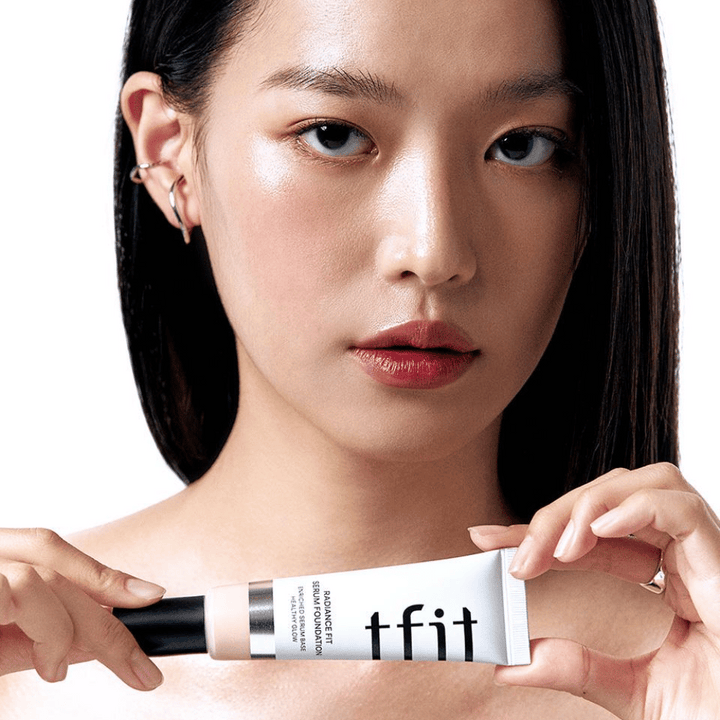 Model z sijočo, gladko kožo drži TFIT Radiance Fit Serum Foundation, kar poudarja naraven zaključek in sijaj izdelka.
