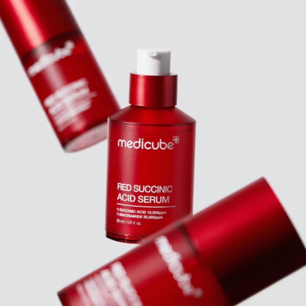 Medicube Red Succinic Acid Serum v rdeči steklenički s pumpico, obdan z več enakimi stekleničkami na svetlem ozadju. Izdelek vsebuje jantarno kislino in niacinamid za zdravljenje aken in pigmentnih madežev.