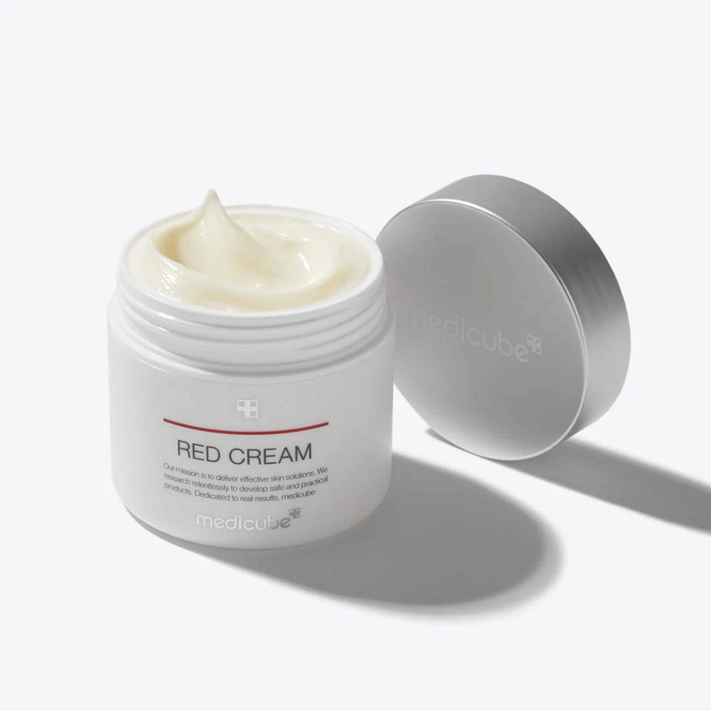 Odprta posoda z medicube Red Cream 50ml – svetlo rumena krema za obraz v beli embalaži s srebrnim pokrovčkom, razvita za kožo, nagnjeno k aknam.