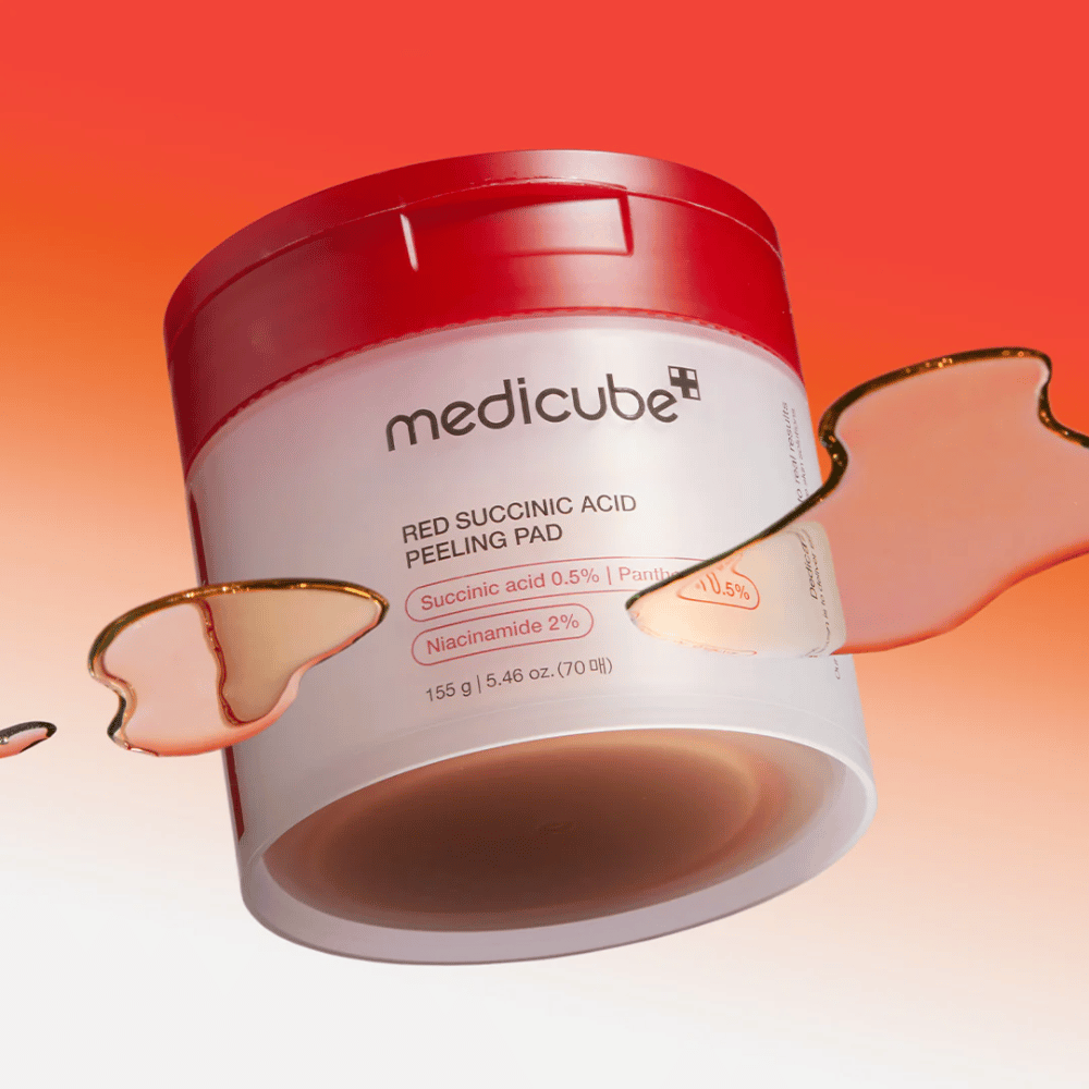 Medicube Red Succinic Acid Peeling Pad v beli in rdeči posodi, postavljena proti gradientnemu ozadju v rdeči in oranžni barvi. Izdelek vsebuje sukcinsko kislino in niacinamid za eksfoliacijo in izboljšanje kože. Tekoča tekstura je vidna okoli posode.