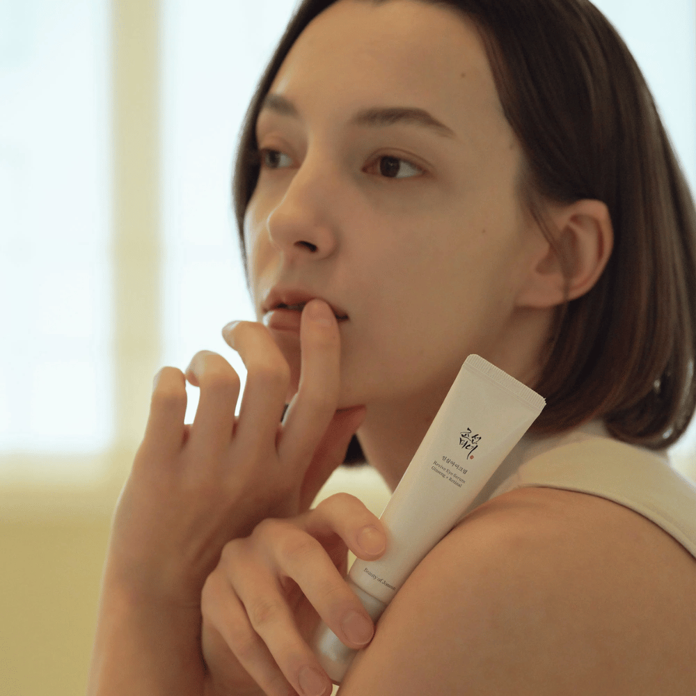 Model drži Beauty of Joseon Revive Eye Serum in ga previdno nanaša na kožo za navlaženo in gladko očesno konturo.
