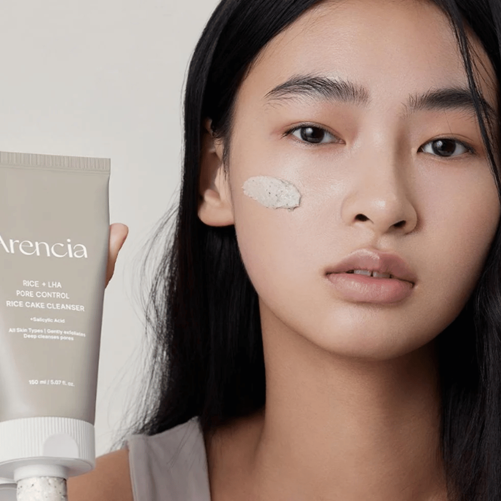 Model, ki drži Arencia Rice + LHA Pore Control Rice Cake Cleanser z naneseno vsebino na licu, prikazuje blag, a učinkovit čistilec por za vsakodnevno uporabo.