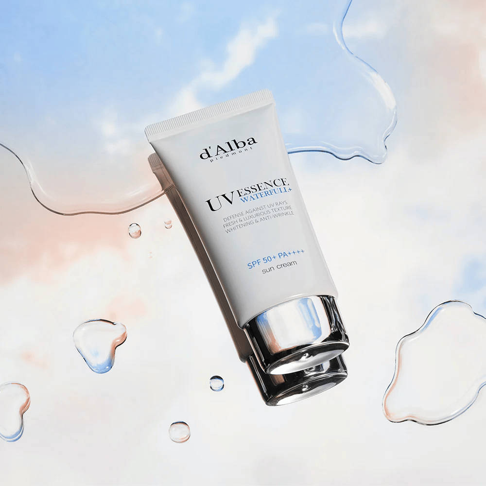 Slika izdelka d'Alba UV Essence Waterfull+ Sun Cream z SPF 50+ PA++++, postavljena na ozadju z vodnimi kapljicami in modro-roza nebom – simbolizira lahko in vlažilno zaščito pred soncem.