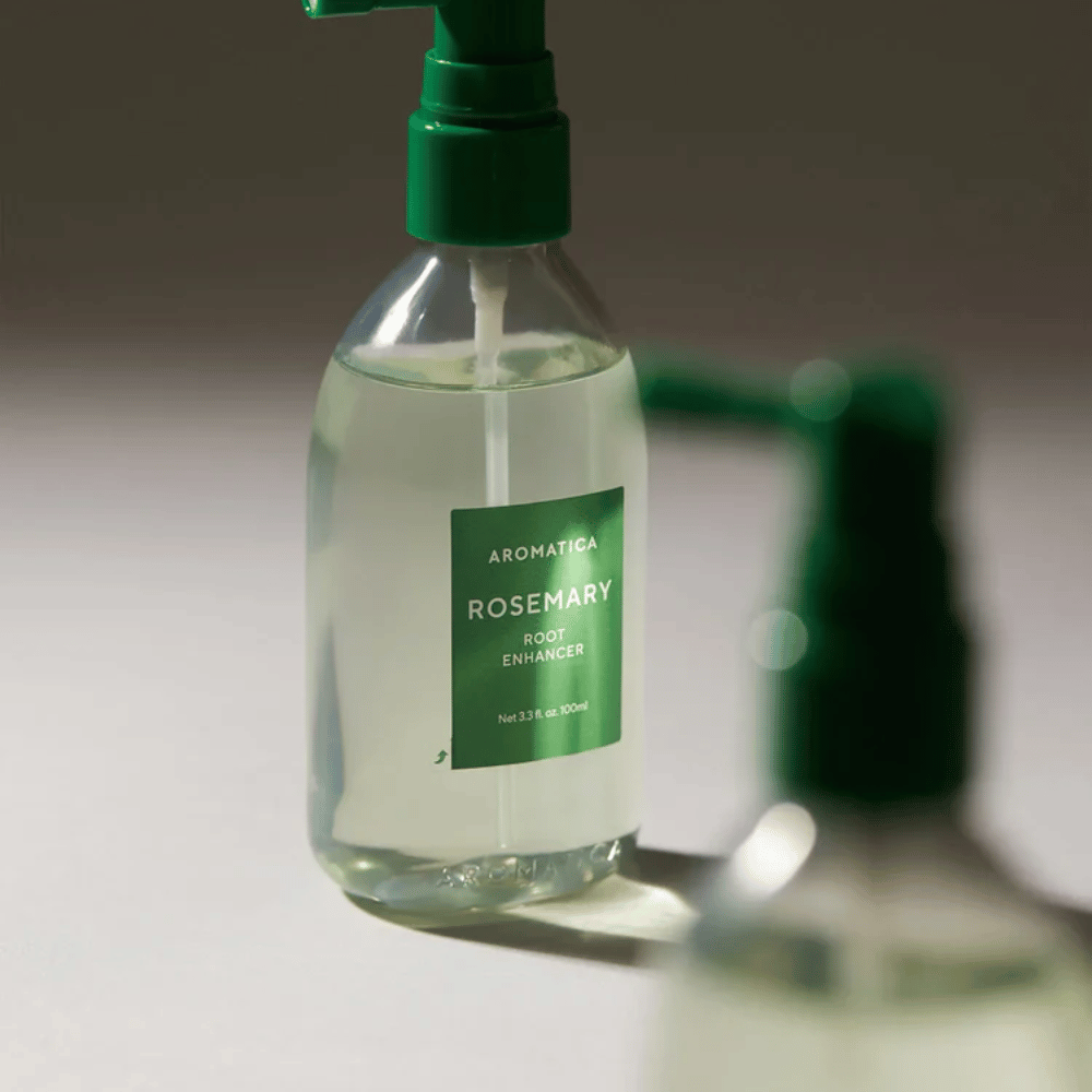 Bližnji posnetek AROMATICA Rosemary Root Enhancer z zelenim aplikatorskim nastavkom. Slika se osredotoča na dizajn stekleničke in natančen nanos neposredno na lasišče.