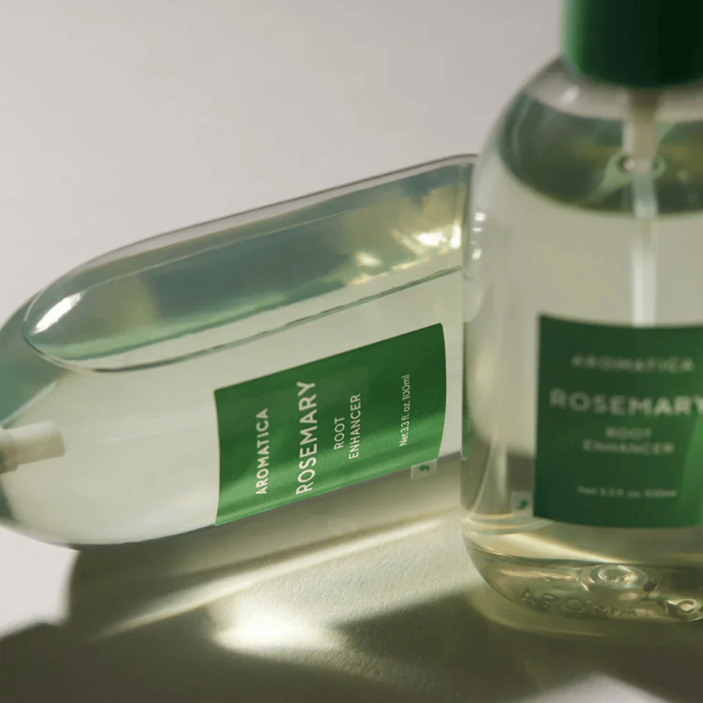 Dve steklenički AROMATICA Rosemary Root Enhancer s prozornim zaščitnim pokrovčkom in zeleno etiketo. Bližnji posnetek, ki poudarja premium dizajn izdelka in koncept naravne nege las.