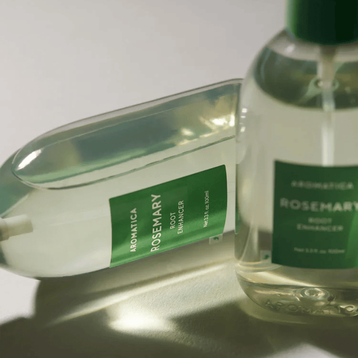 Dve steklenički AROMATICA Rosemary Root Enhancer s prozornim zaščitnim pokrovčkom in zeleno etiketo. Bližnji posnetek, ki poudarja premium dizajn izdelka in koncept naravne nege las.