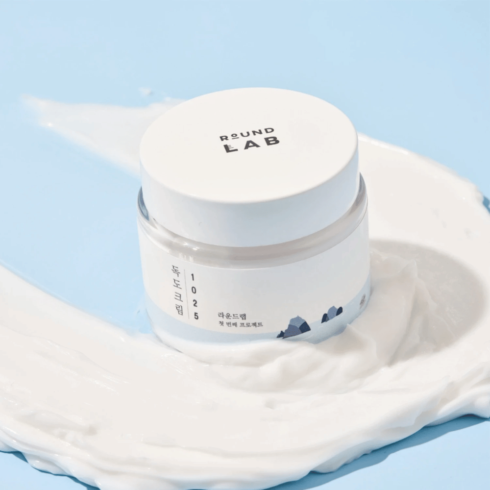 Kozarec z Round Labs 1025 Dokdo Cream 80 ml, ki zagotavlja vlaženje, postavljen na živahno modro ozadje.