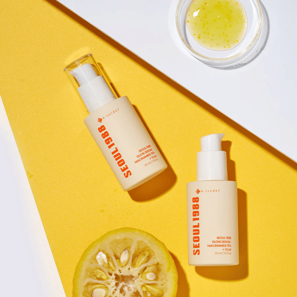Dve steklenici Seoul 1988 Glow Serum, postavljeni na rumeno ozadje skupaj s skledo rumenega seruma in prepolovljenim citrusom.