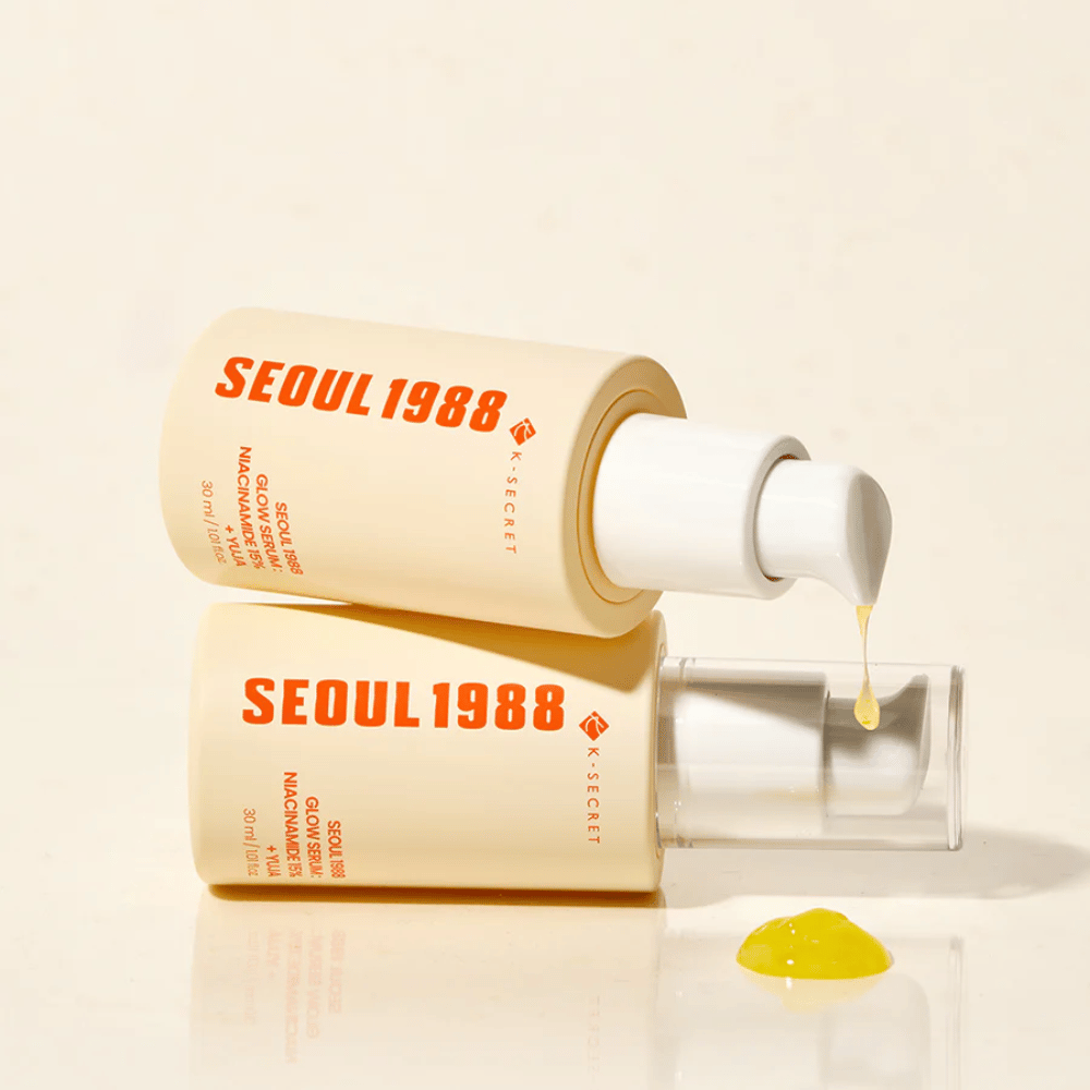 Dve steklenici Seoul 1988 Glow Serum ležita in stojita, z rumenim serumom, ki kaplja iz črpalke.