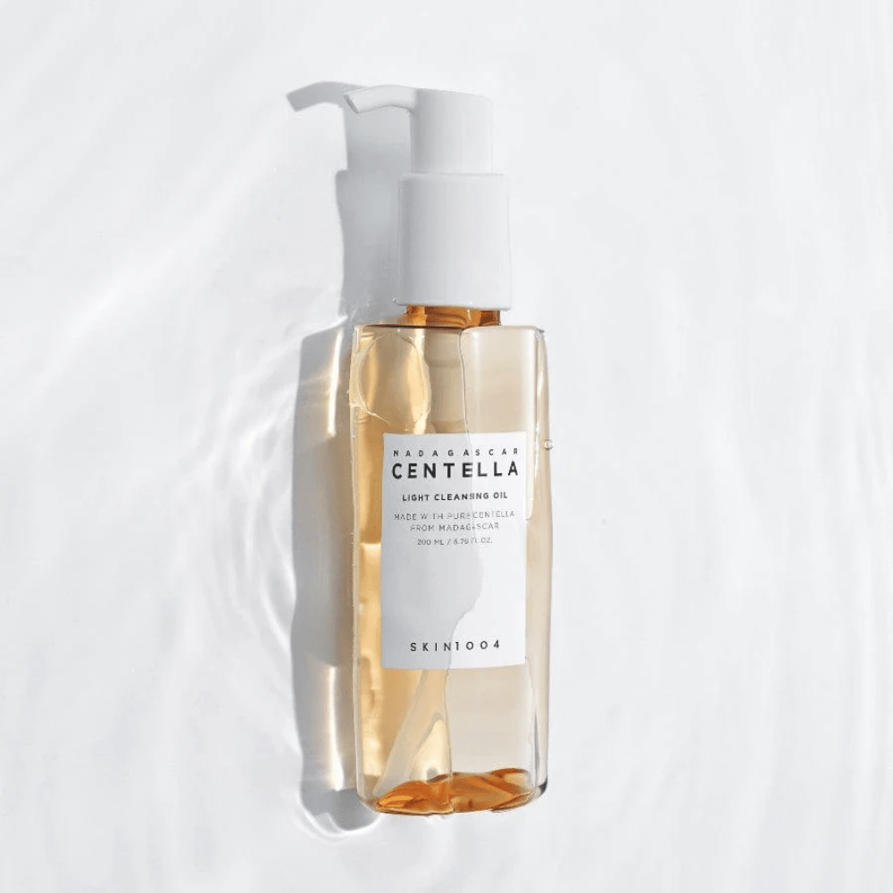 SKIN1004 Madagascar Centella Light Cleansing Oil na beli podlagi z mehkimi vodnimi odsevi, ki poudarjajo prozorno stekleničko in zlato vsebino.