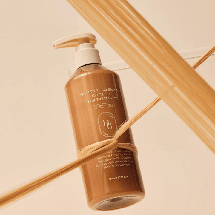 Heveblue Salmon Pullkeratin Centella Hair Treatment v rjavi steklenički, obdani s prameni las. Slika poudarja negovalne lastnosti tretmaja za lase s poudarkom na sijaju, moči in svilnato gladkih laseh.