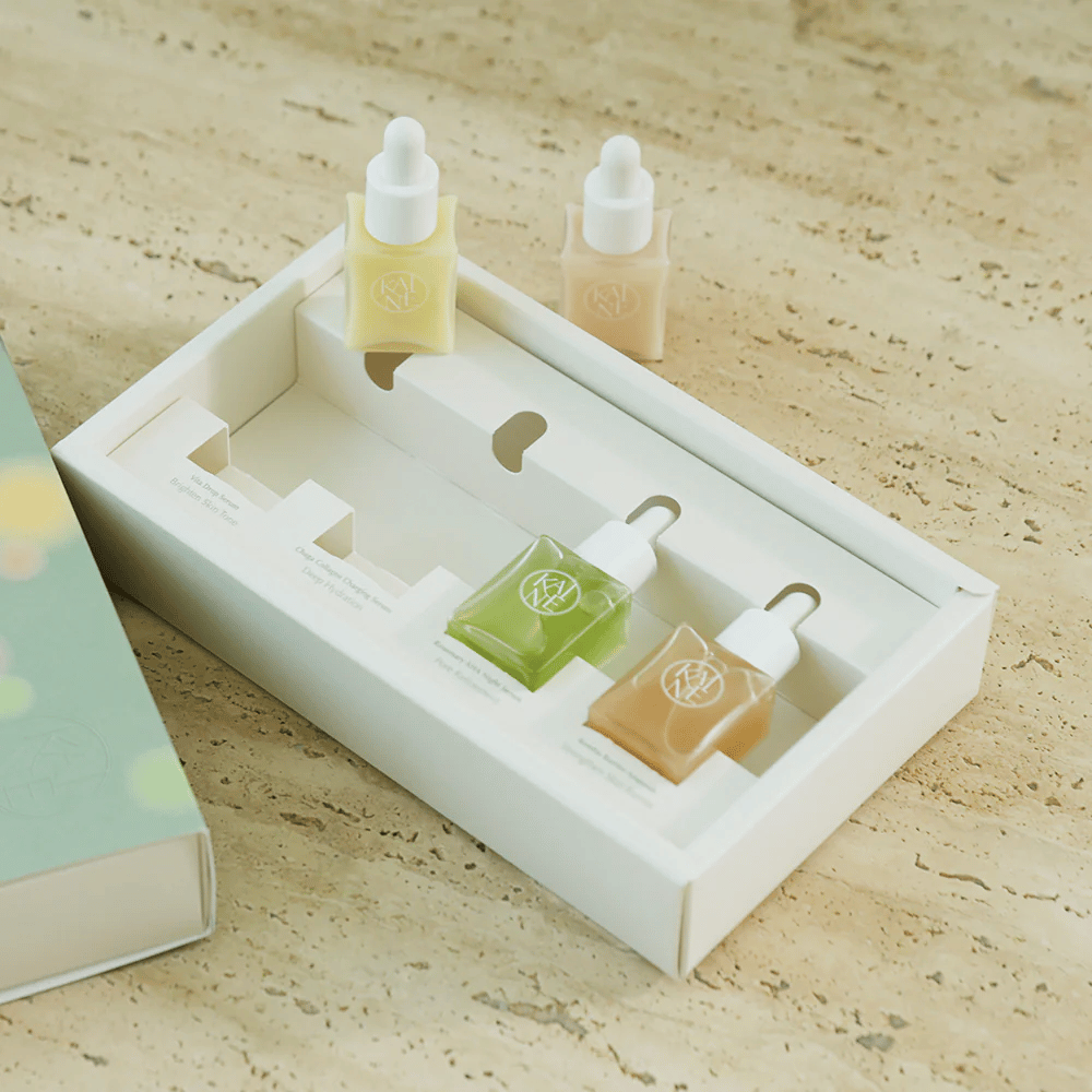 Štiri barvne stekleničke s serumom iz KAINE Serum Discovery Kit z zamaškom pipete, zasnovane za zadovoljevanje različnih potreb kože v minimalistični in elegantni embalaži.