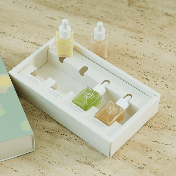 Štiri barvne stekleničke s serumom iz KAINE Serum Discovery Kit z zamaškom pipete, zasnovane za zadovoljevanje različnih potreb kože v minimalistični in elegantni embalaži.