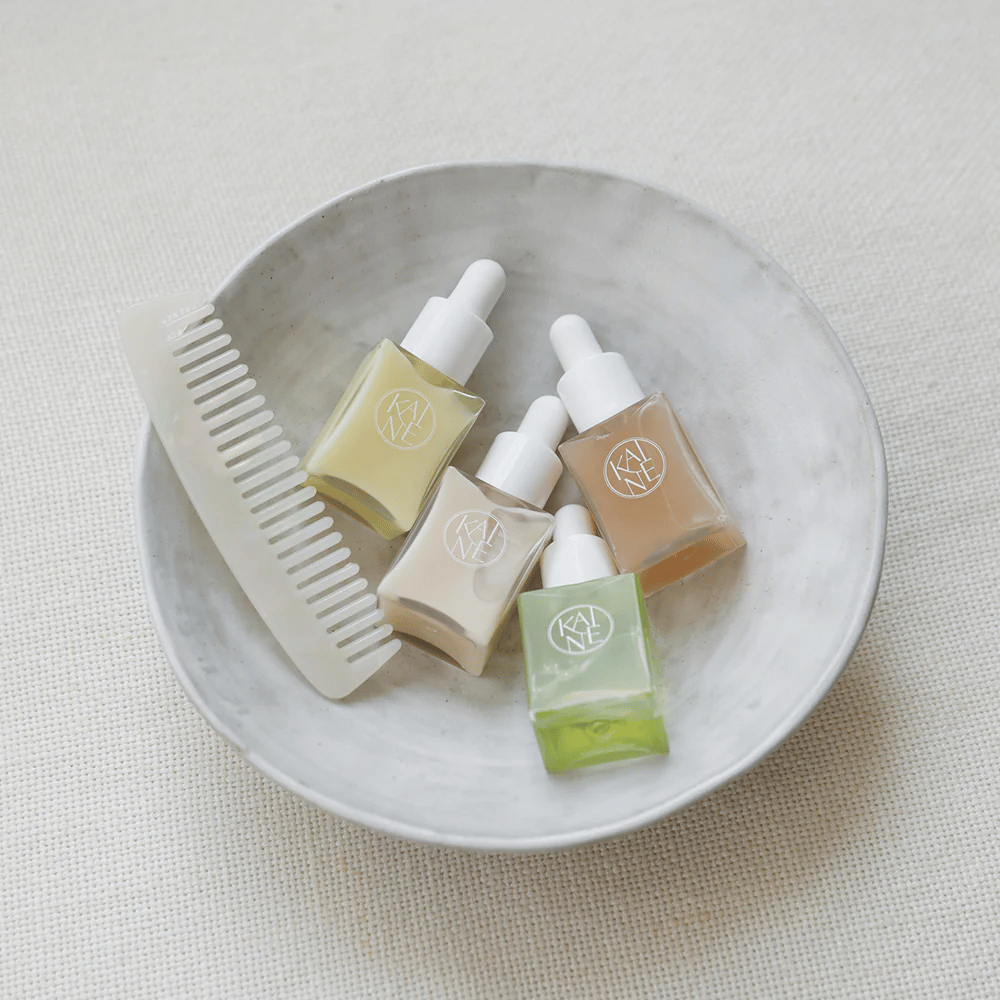 Štiri majhne stekleničke s serumom iz KAINÉ Serum Discovery Kit ležijo v beli skledi poleg glavnika, z naravnim in mirnim ozadjem v bež tonu.