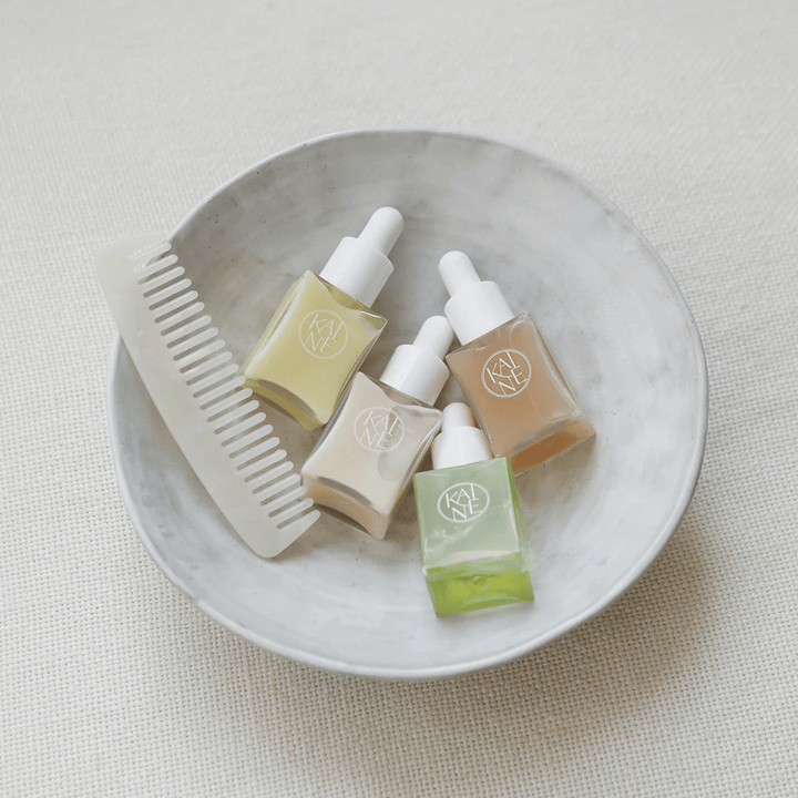 Štiri majhne stekleničke s serumom iz KAINÉ Serum Discovery Kit ležijo v beli skledi poleg glavnika, z naravnim in mirnim ozadjem v bež tonu.