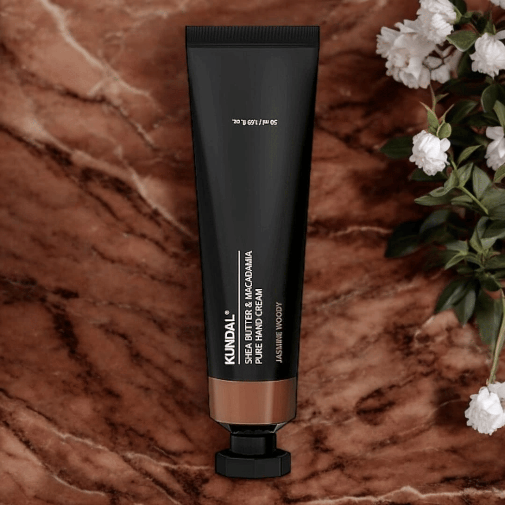 KUNDAL Shea Butter & Macadamia Pure Hand Cream Jasmine Woody postavljena na marmor z rožami – hranilna krema za roke, ki neguje suhe roke in daje eleganten vonj jasmine woody.