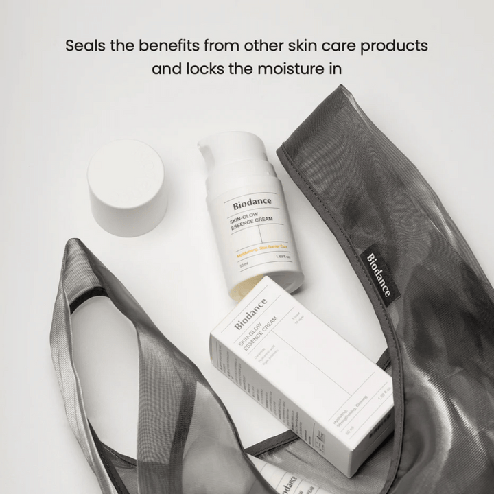 Biodance Skin-Glow Essence Cream stoji v ospredju skupaj z embalažo izdelka in črno prozorno toaletno torbico, z besedilom nad njo, ki poudarja sposobnost kreme, da zadrži vlago in okrepi učinek drugih izdelkov za nego kože.