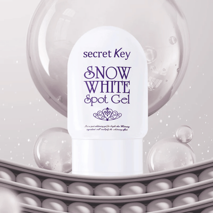 Secret Key Snow White Spot Gel v beli embalaži na ozadju z mehurčki in bisernimi detajli.