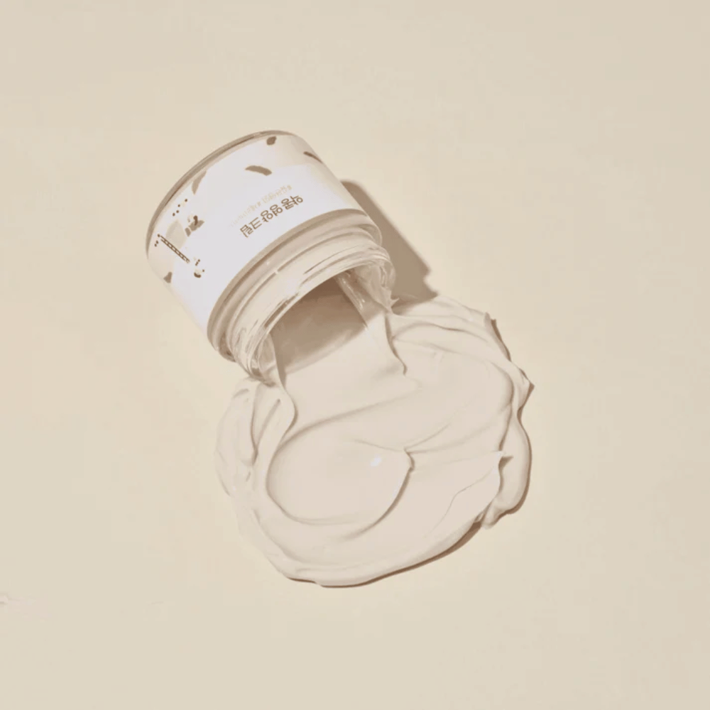 Mixsoon Soybean Nourishing Cream razlita iz posode na bež ozadju. Bogata konsistenca kreme kaže na njene intenzivne vlažilne lastnosti.